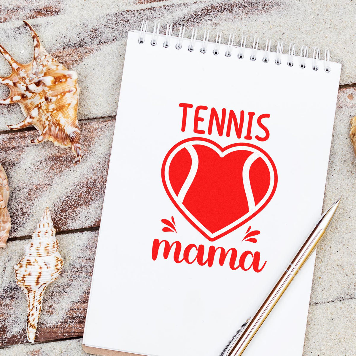 Red tennis-ball heart mama stamp and seal on white spiral notebook, with seashells and a gold pen.