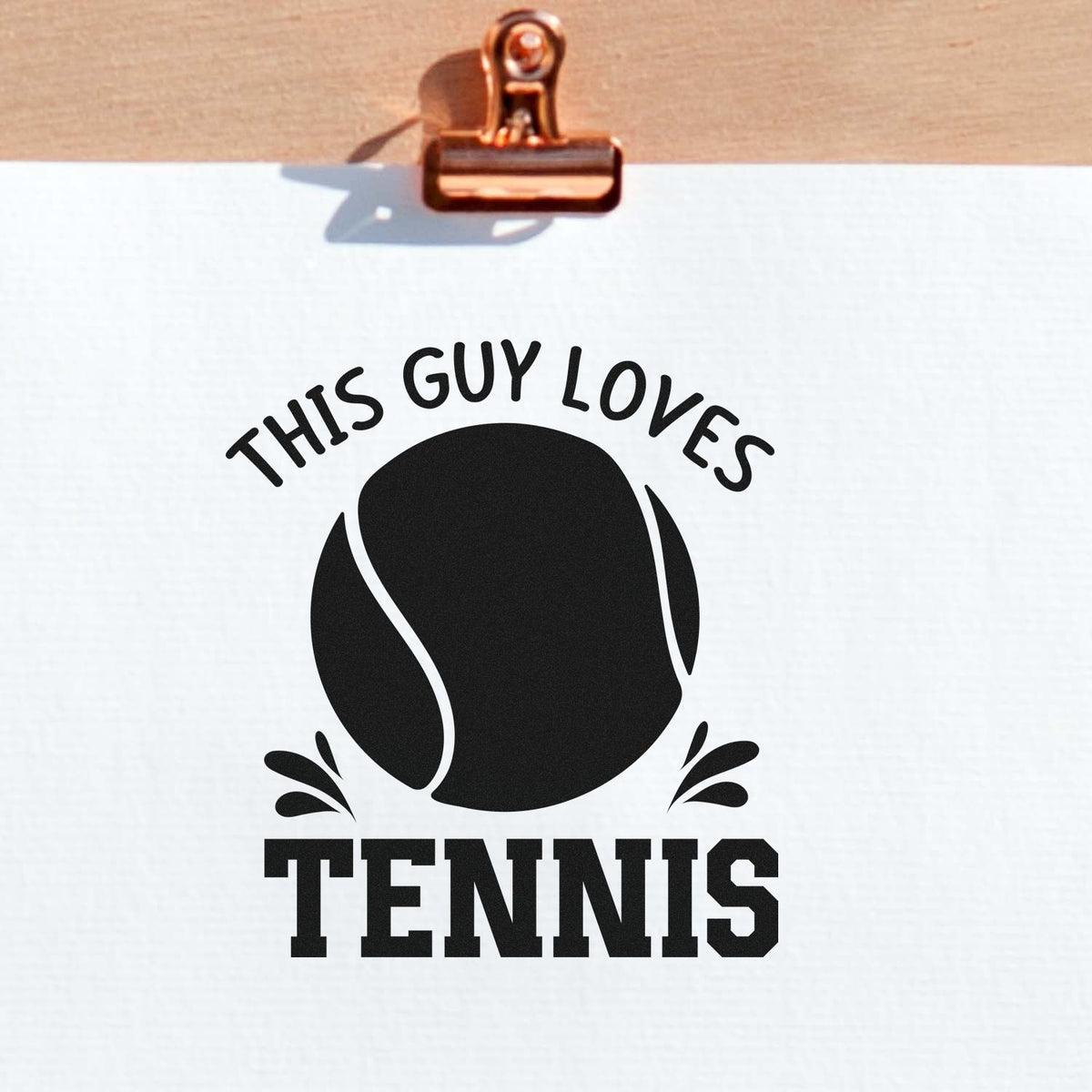 Copper clip holding white paper with a black tennis stamp seal reading THIS GUY LOVES TENNIS and a tennis ball icon.