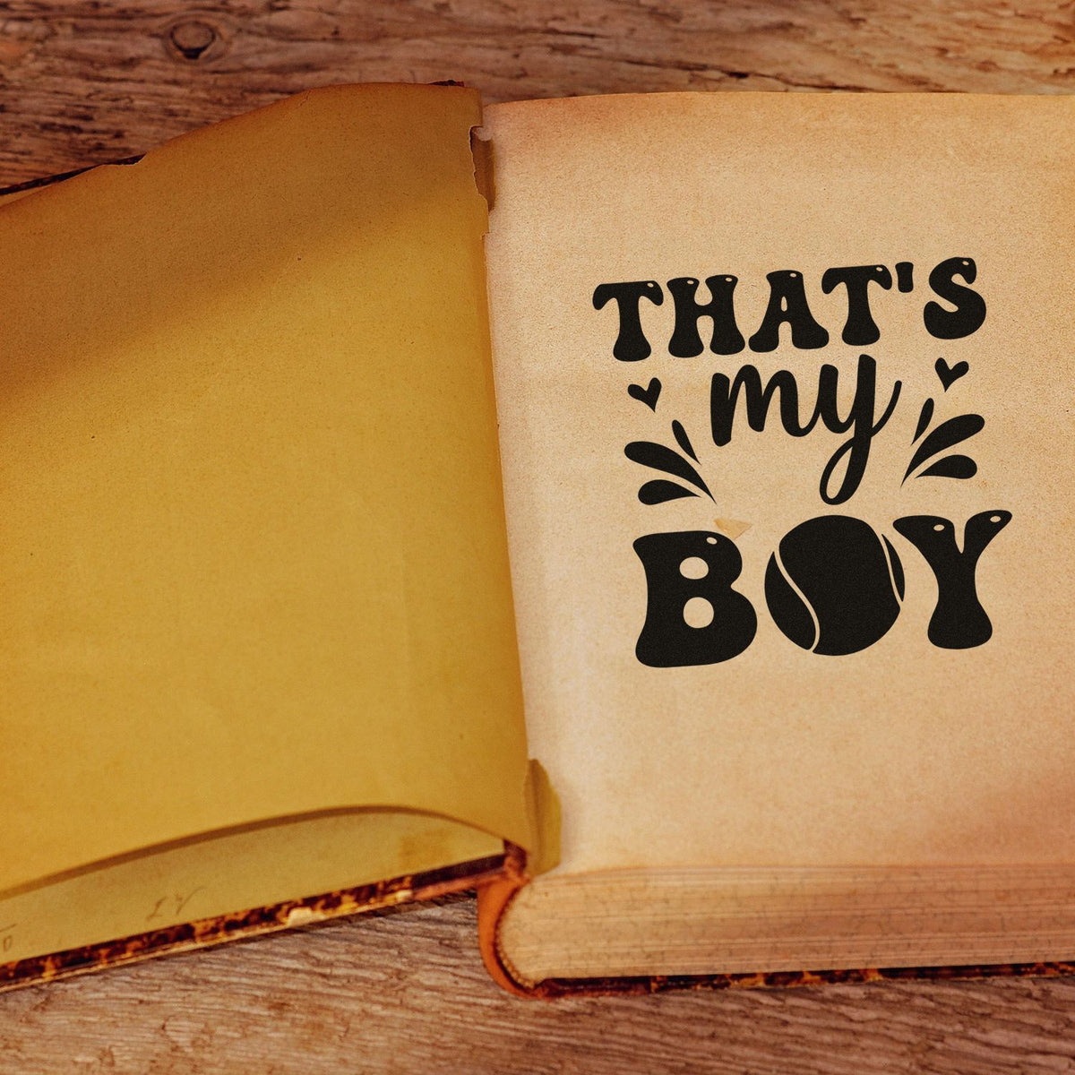 Open book with black custom stamp and seal reading Thats my boy on beige pages over rustic wood.