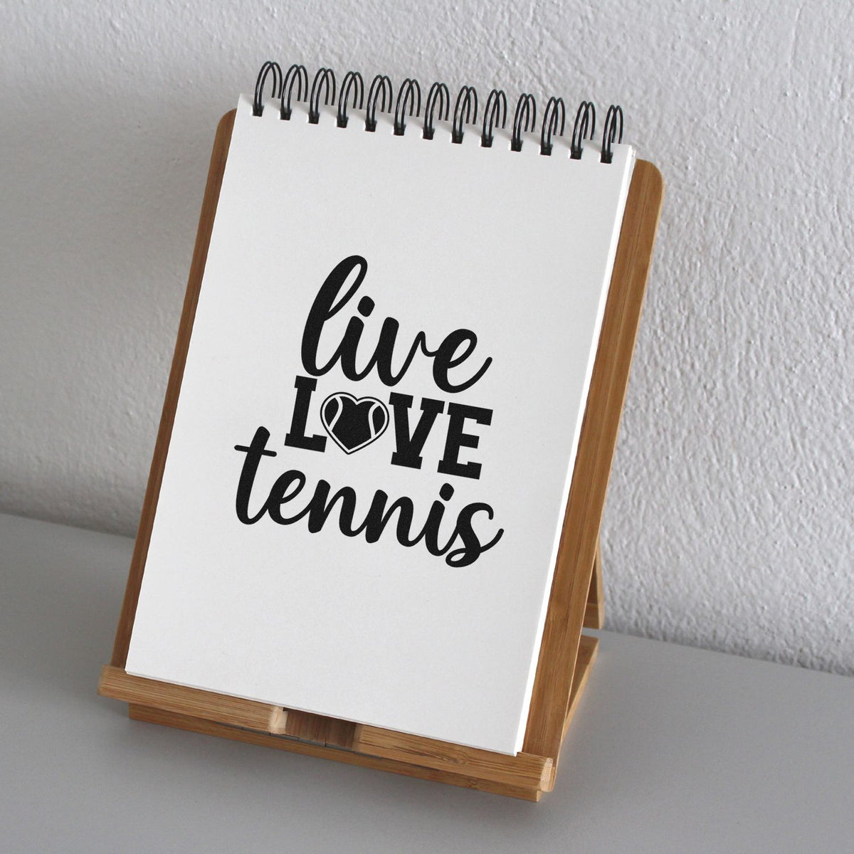 Custom black stamp design reading live love tennis on a white spiral pad in a wooden display stand.