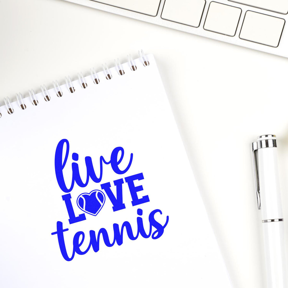 Blue custom stamp/seal on white notebook: Live Love Tennis with heart icon, beside a white pen.