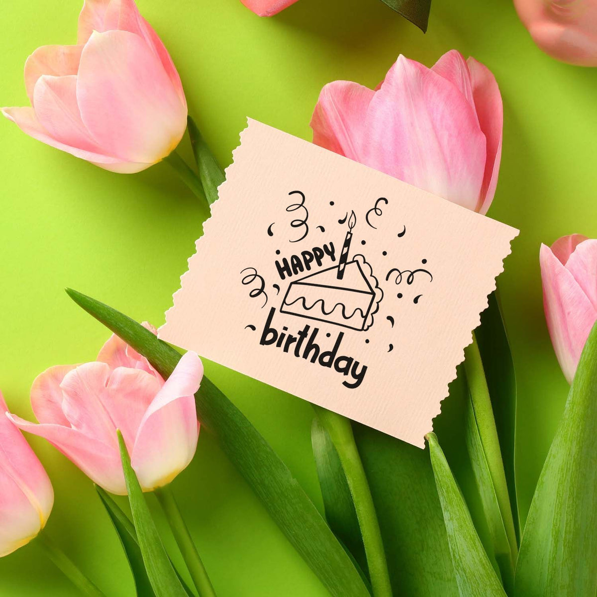 Black Happy Birthday cake stamp and seal on beige textured paper, framed by pink tulips on a bright green background.