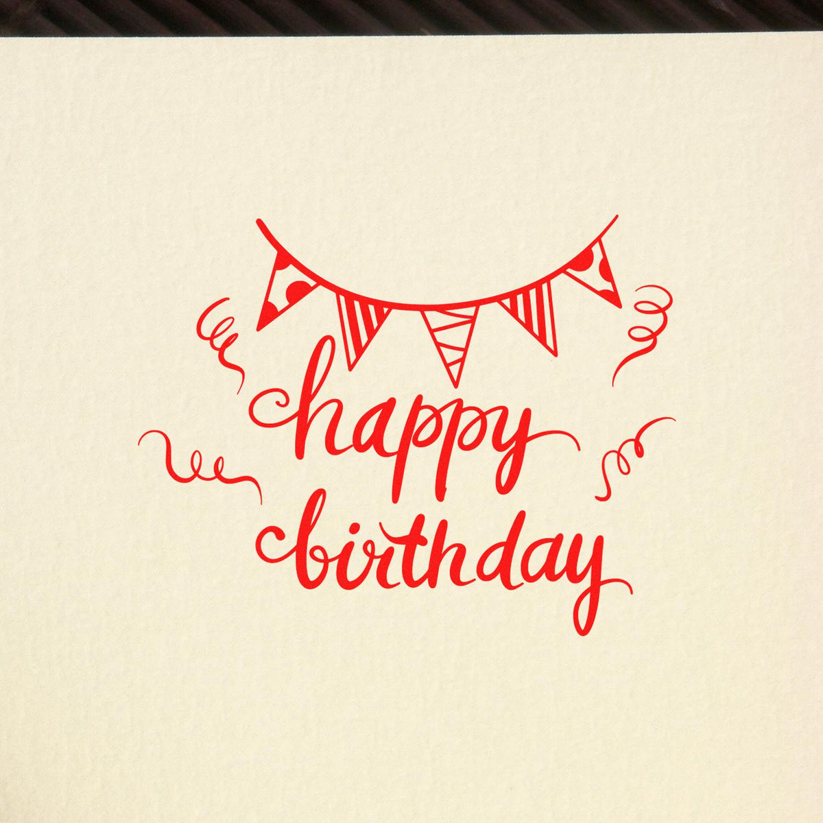 Red birthday stamp seal with bunting and confetti on cream background, reading happy birthday