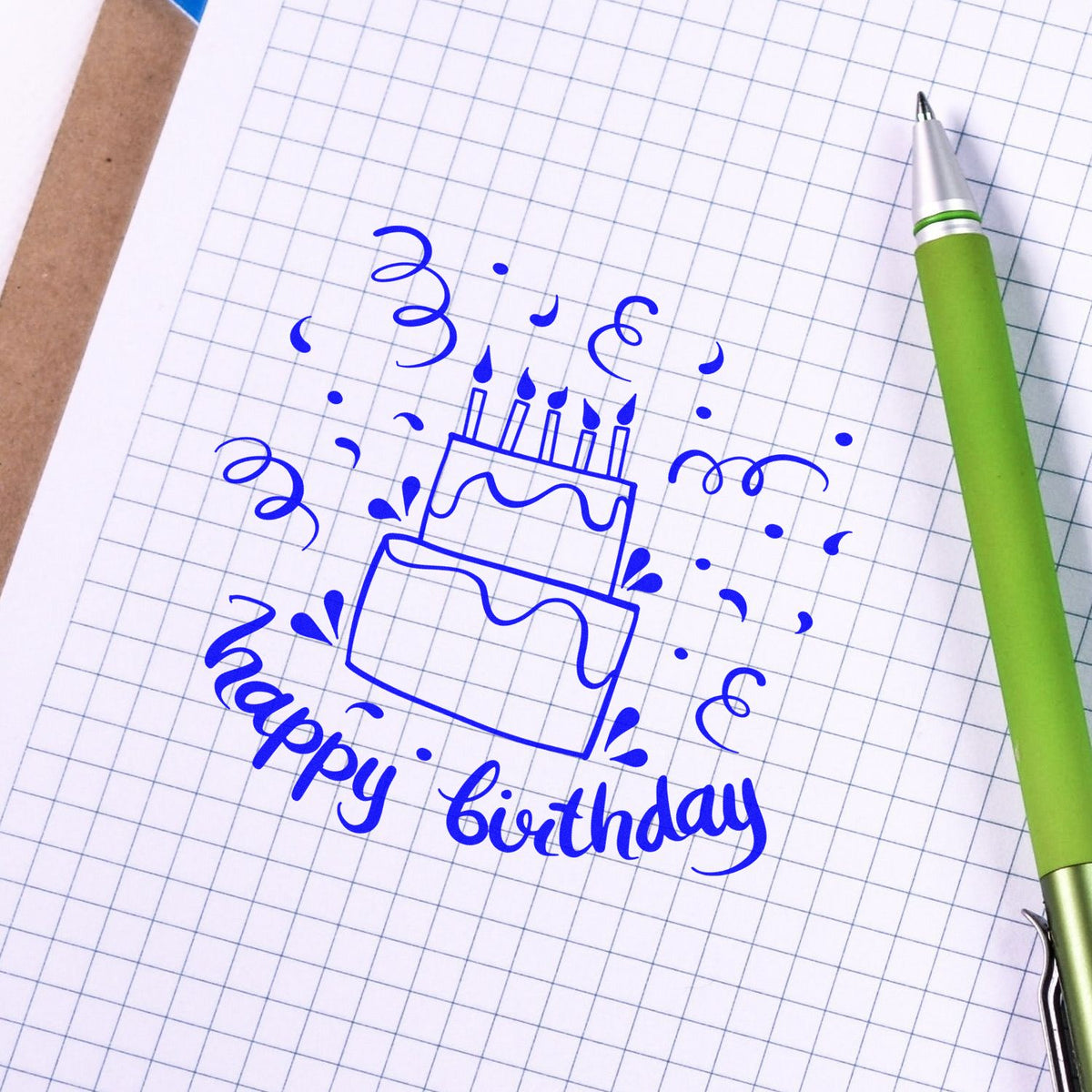 Blue birthday cake stamp design on graph paper with confetti and a green pen, for stamp and seal products.