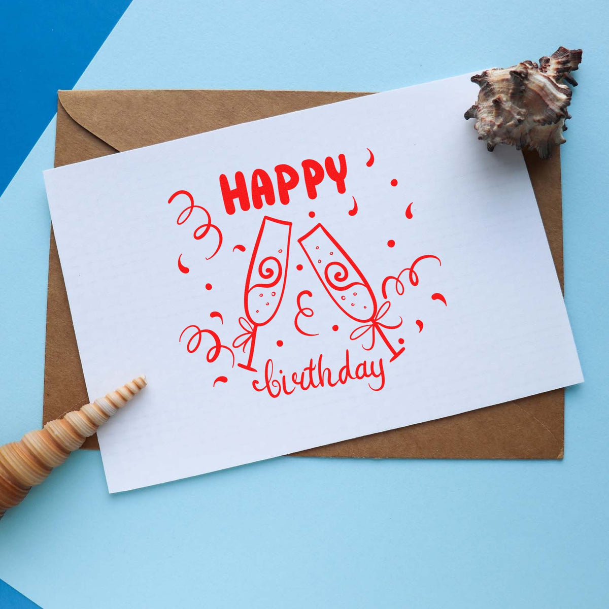 Red happy birthday stamp on white card with champagne glasses, on brown envelope against blue background, sealed with seashells.
