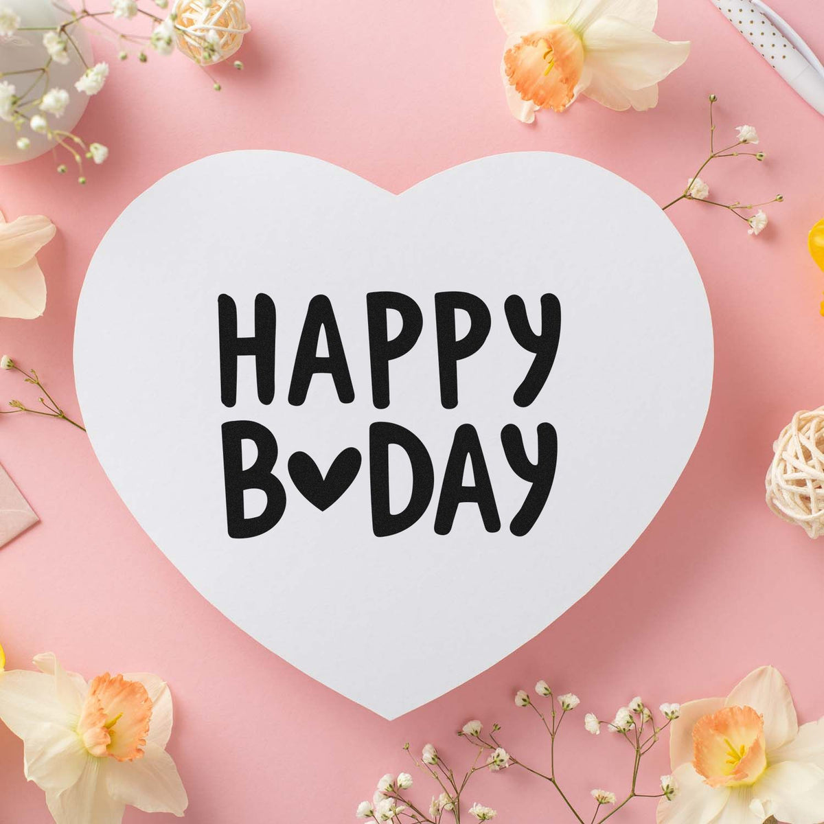 Heart-shaped white birthday seal stamp with black HAPPY BDAY text on a pink floral background.
