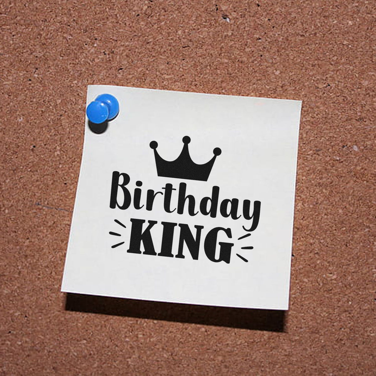 Black Birthday King stamp seal on white paper, pinned with blue tacks against a brown corkboard.