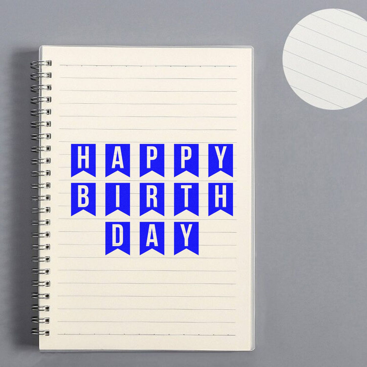 Blue HAPPY BIRTH DAY stamp on cream spiral notebook, with round lined seal paper in the corner.