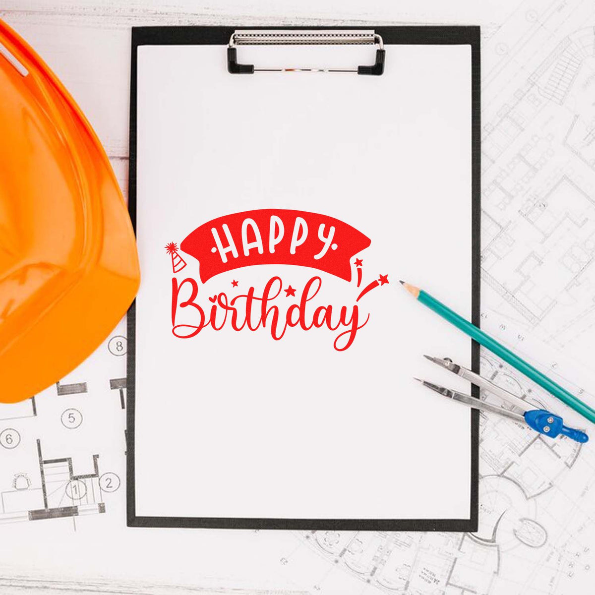 Red Happy Birthday stamp on a clipboard with orange hard hat, pencils, and architectural blueprints.