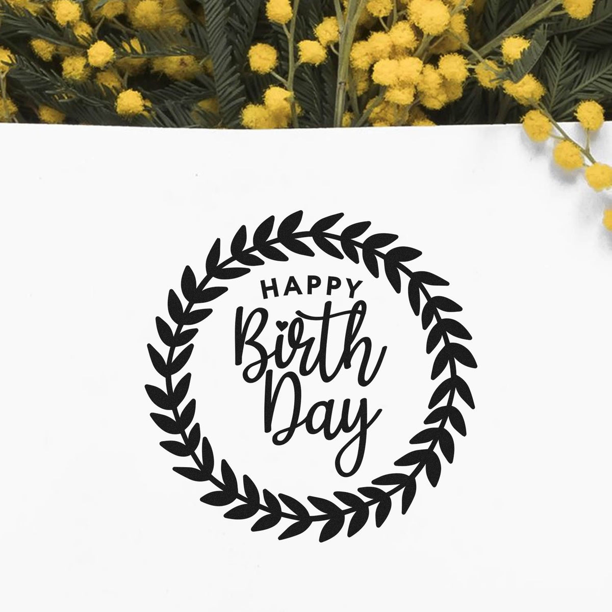 Black Happy Birth Day stamp seal with leafy wreath on white background, framed by yellow flowers and green foliage.