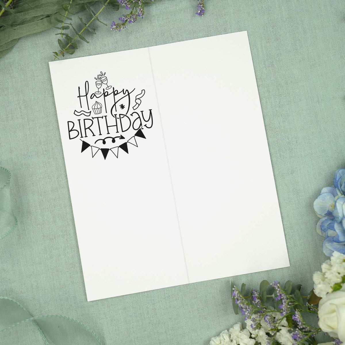Black Happy Birthday stamp with bunting and cake on a white card, styled on a soft green floral background.