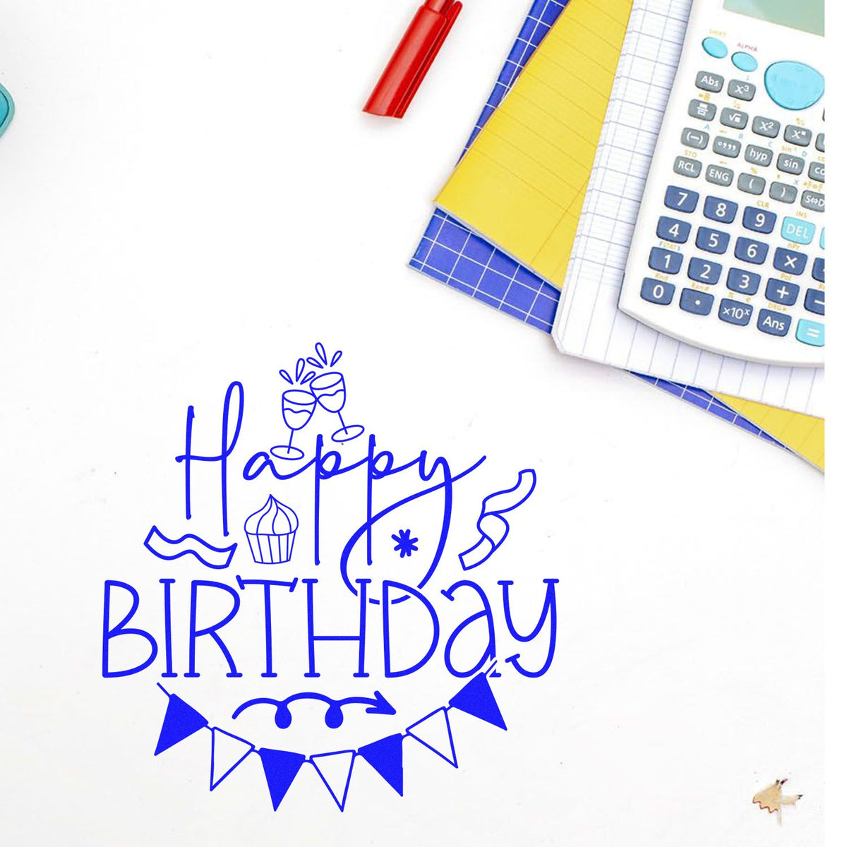 Blue Happy Birthday stamp and seal design with bunting, cupcake, and champagne glasses beside calculator, notebooks, and red pen.