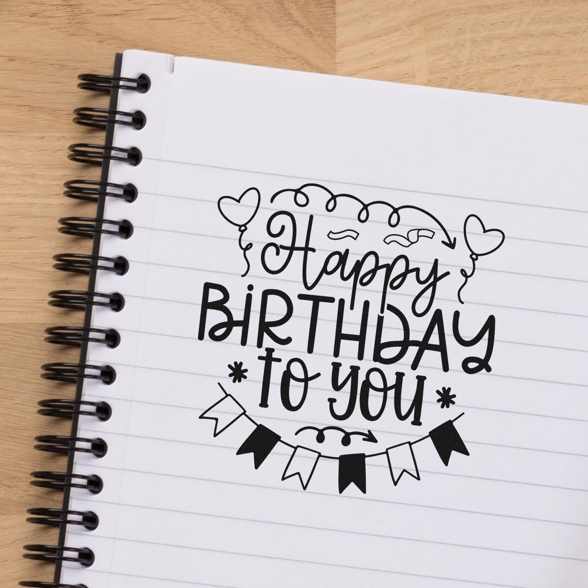 Black stamp-and-seal birthday design on white lined notebook page, with hearts, bunting flags, and Happy Birthday to you lettering.