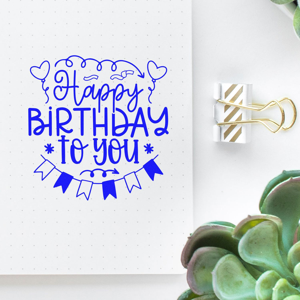Blue Happy Birthday to You stamp and seal design with hearts and bunting on dotted paper, clipped with a gold binder clip.