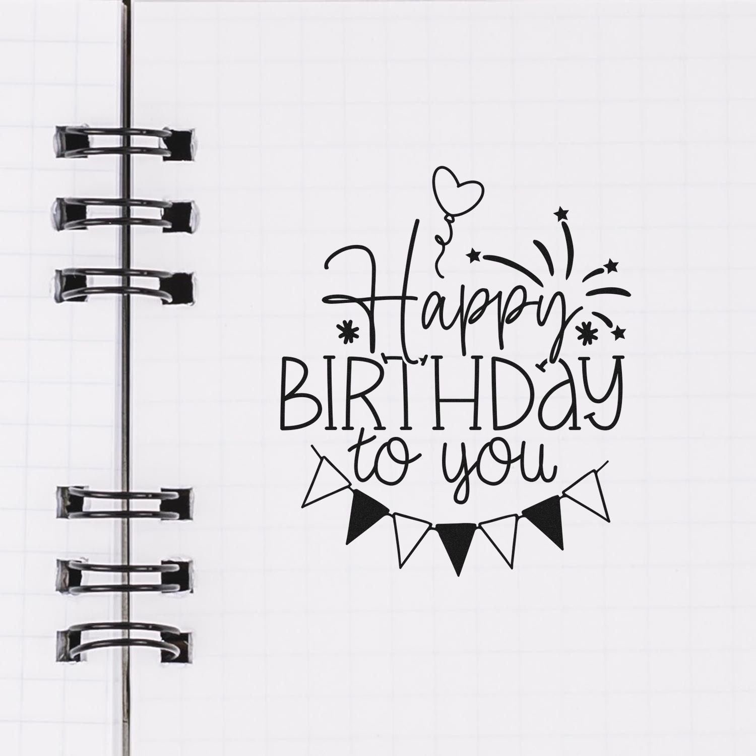 Black Happy Birthday to You stamp and seal design with heart balloon, stars, and bunting on a white spiral notebook page.