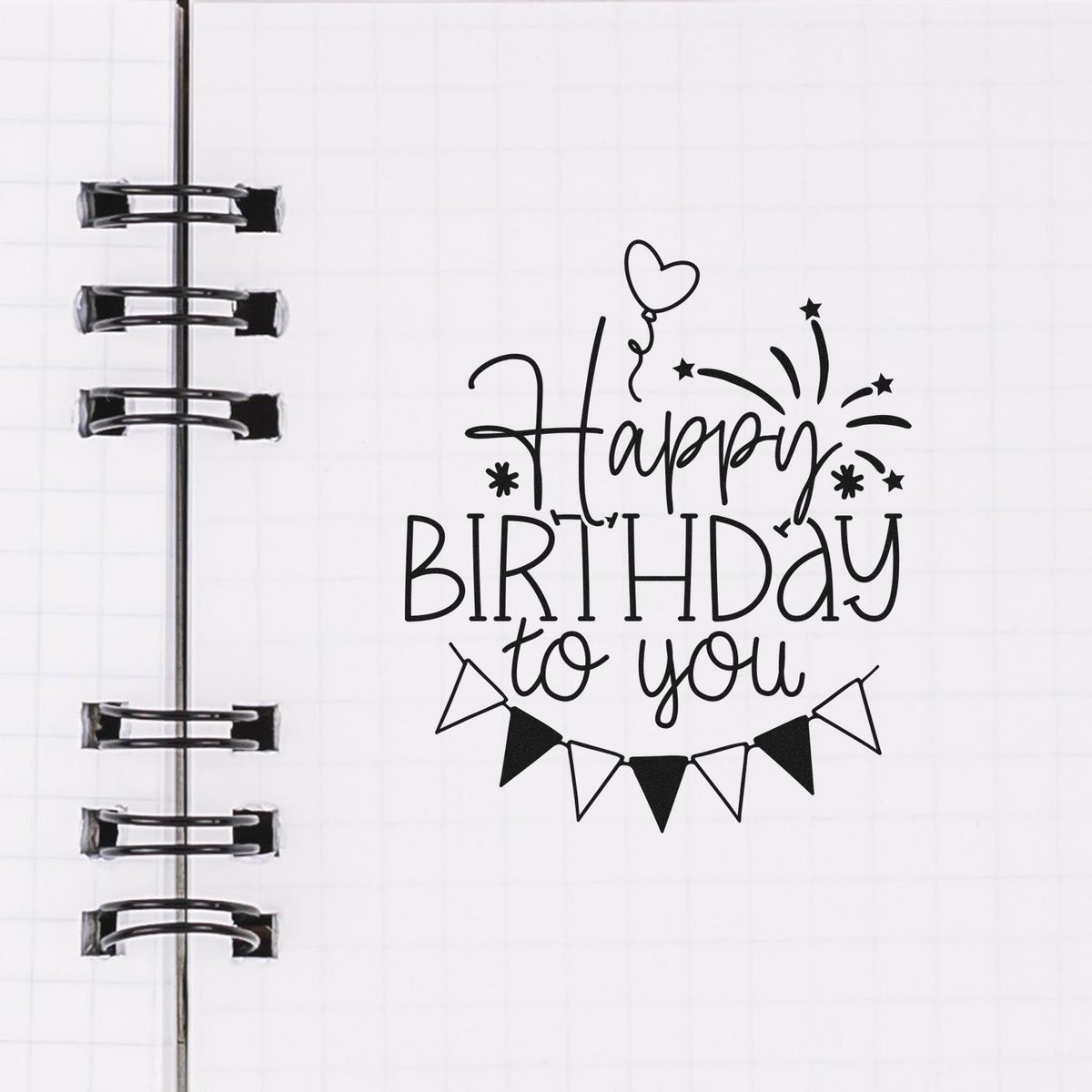 Black Happy Birthday to you stamp and seal design with balloons and bunting on a white notebook page with binder rings.