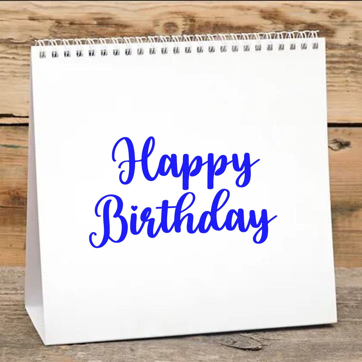 White spiral gift bag with blue Happy Birthday stamp and seal design on rustic wood background.