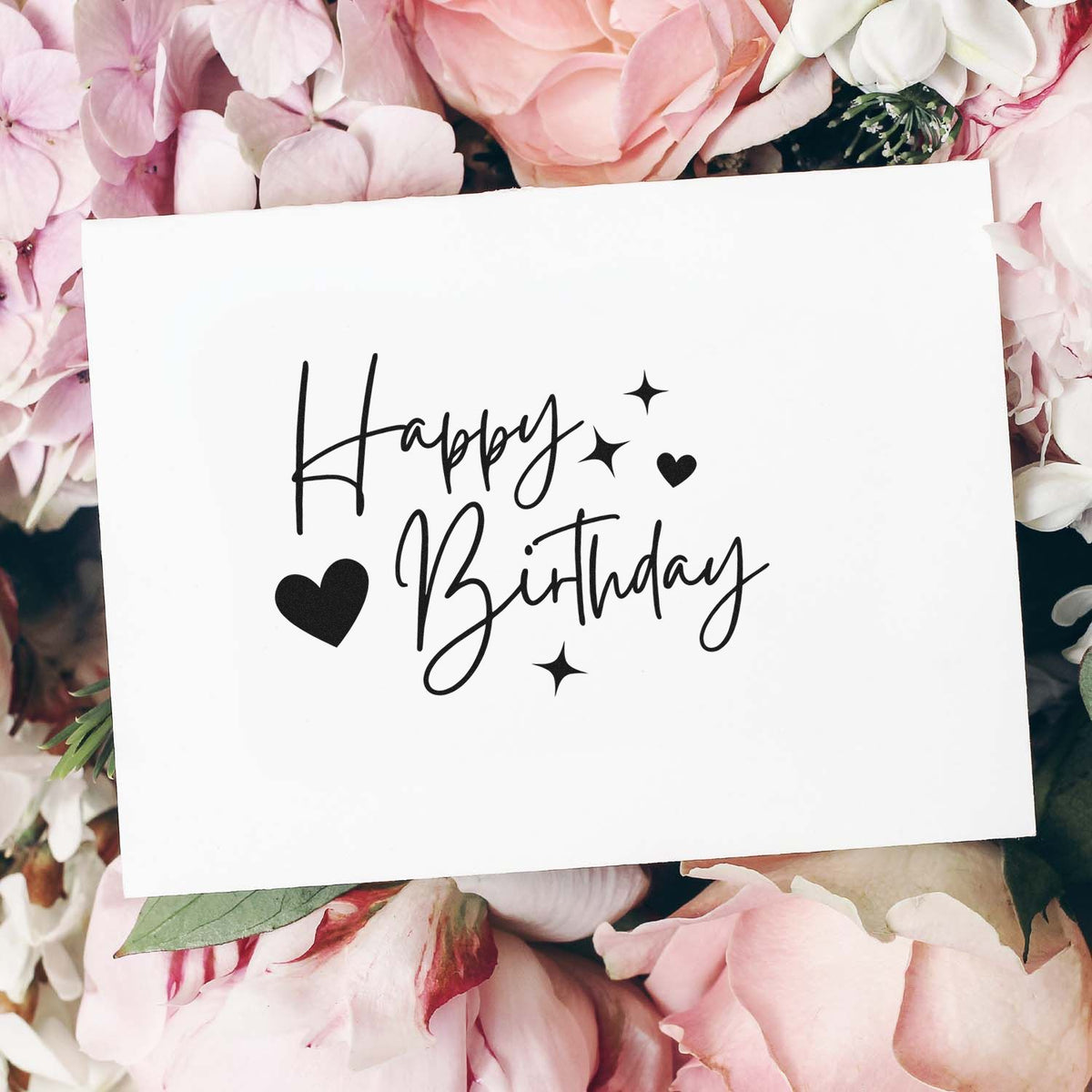 White custom stamp and seal card with black Happy Birthday script, hearts and stars on soft pink flowers.