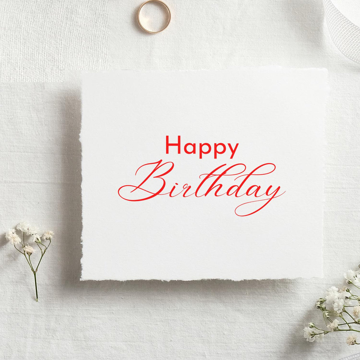 Red Happy Birthday stamp seal on white textured paper, styled with delicate white flowers and a soft neutral background.