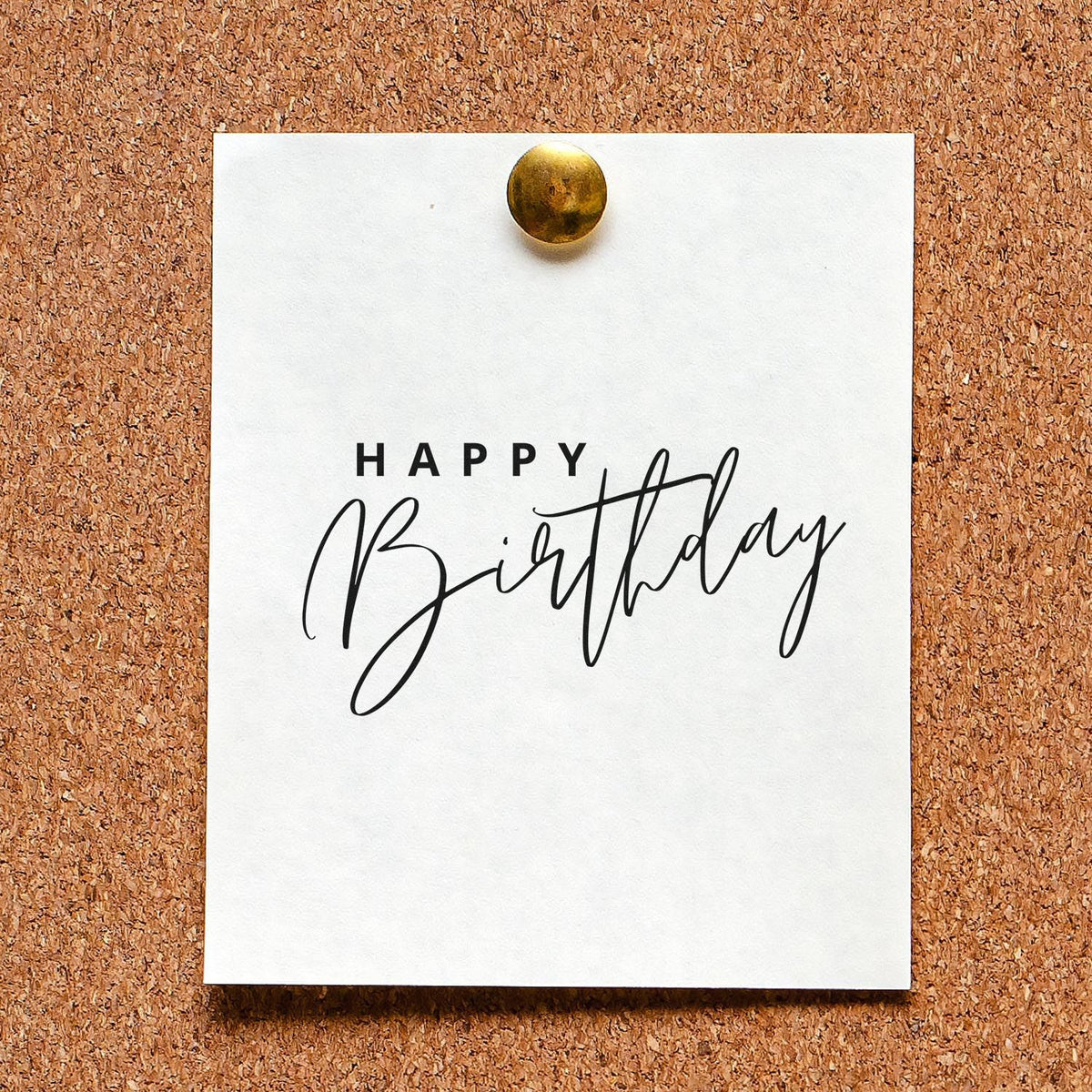 White Happy Birthday stamp and seal card pinned to corkboard with brass tack, black script lettering.