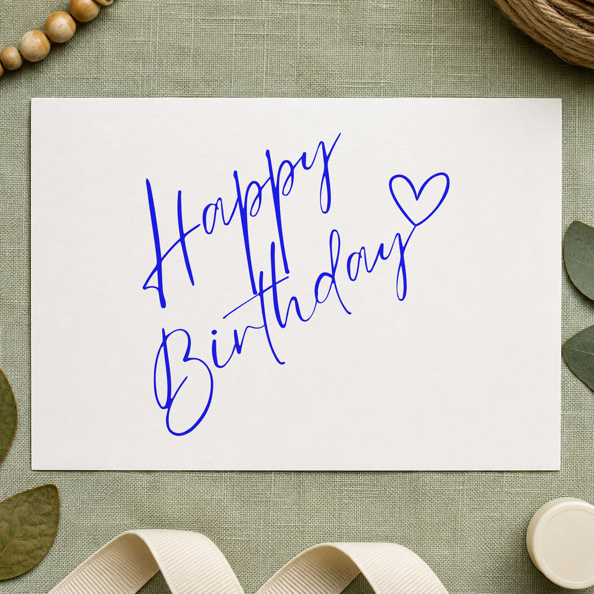 Diagonal Birthday Heart Script craft stamp imprinted in blue ink on paper, a design suited to framed reading chair.