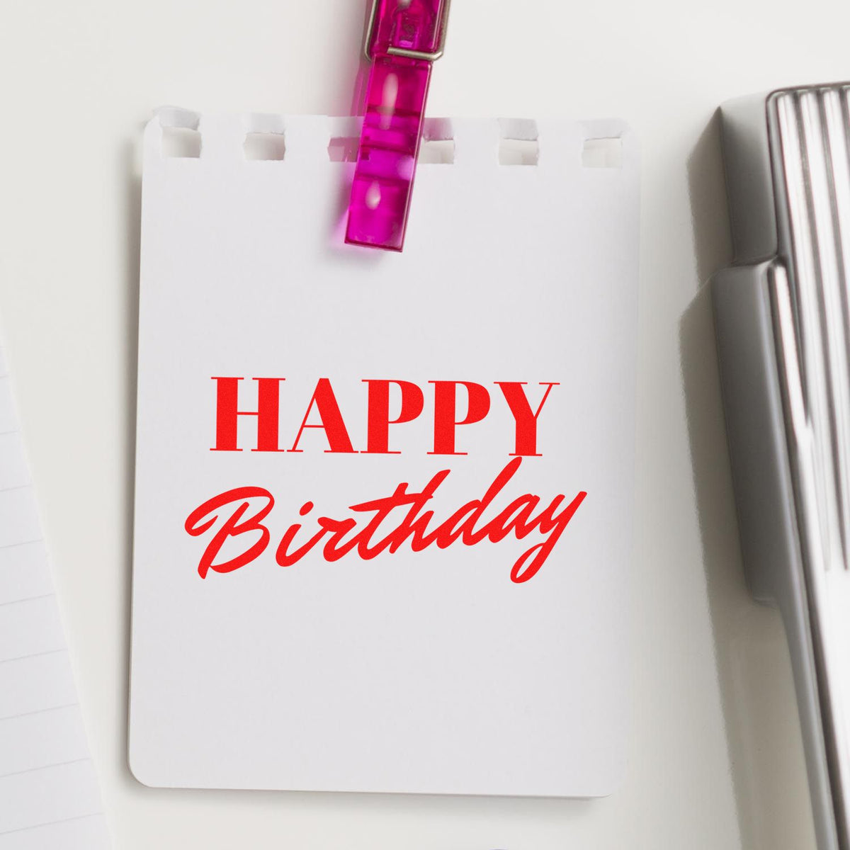 White birthday card with red Happy Birthday text, clipped by a pink seal clip beside a silver stamp tool.