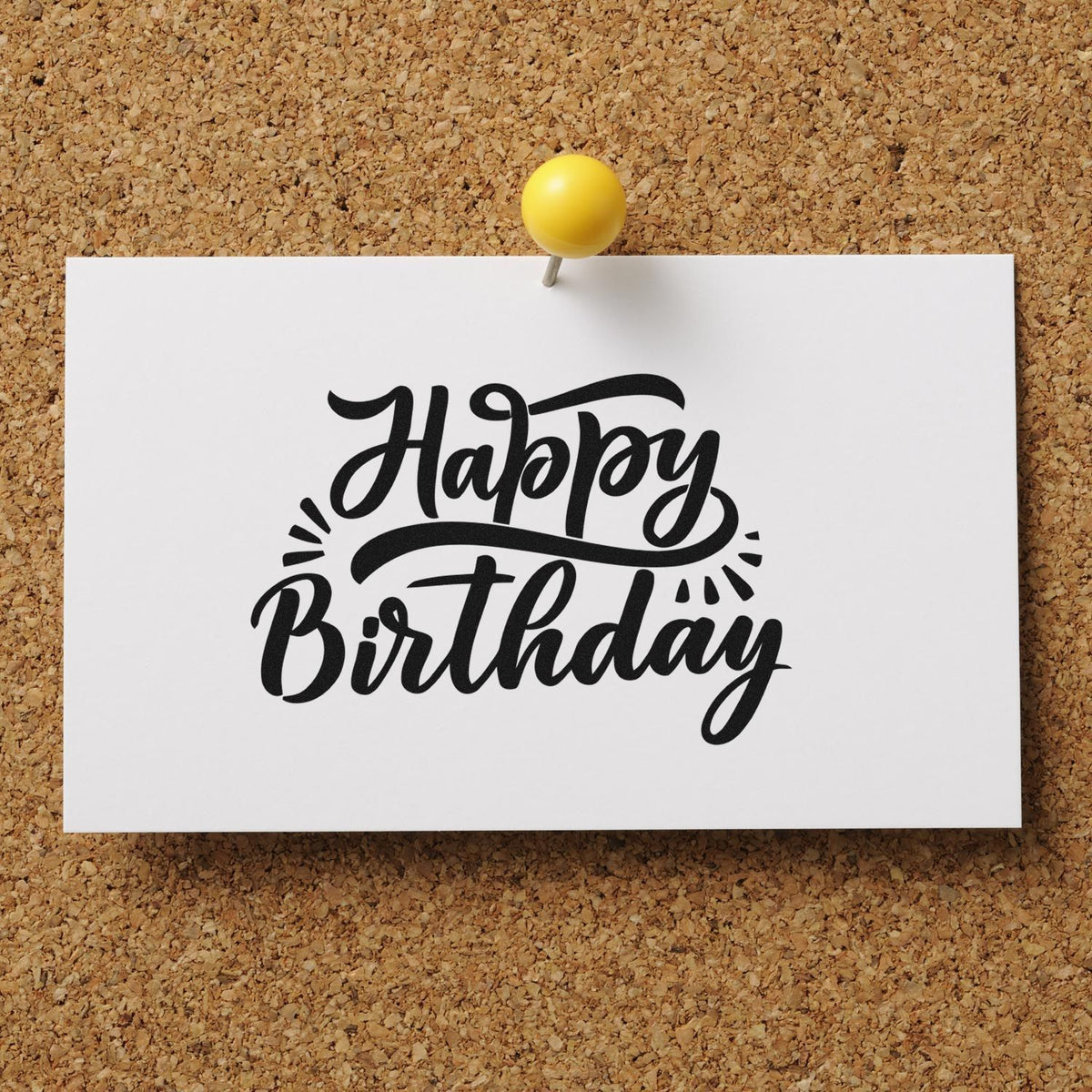 Black Happy Birthday stamp and seal design in black on white card, pinned with a yellow tack against a corkboard background.