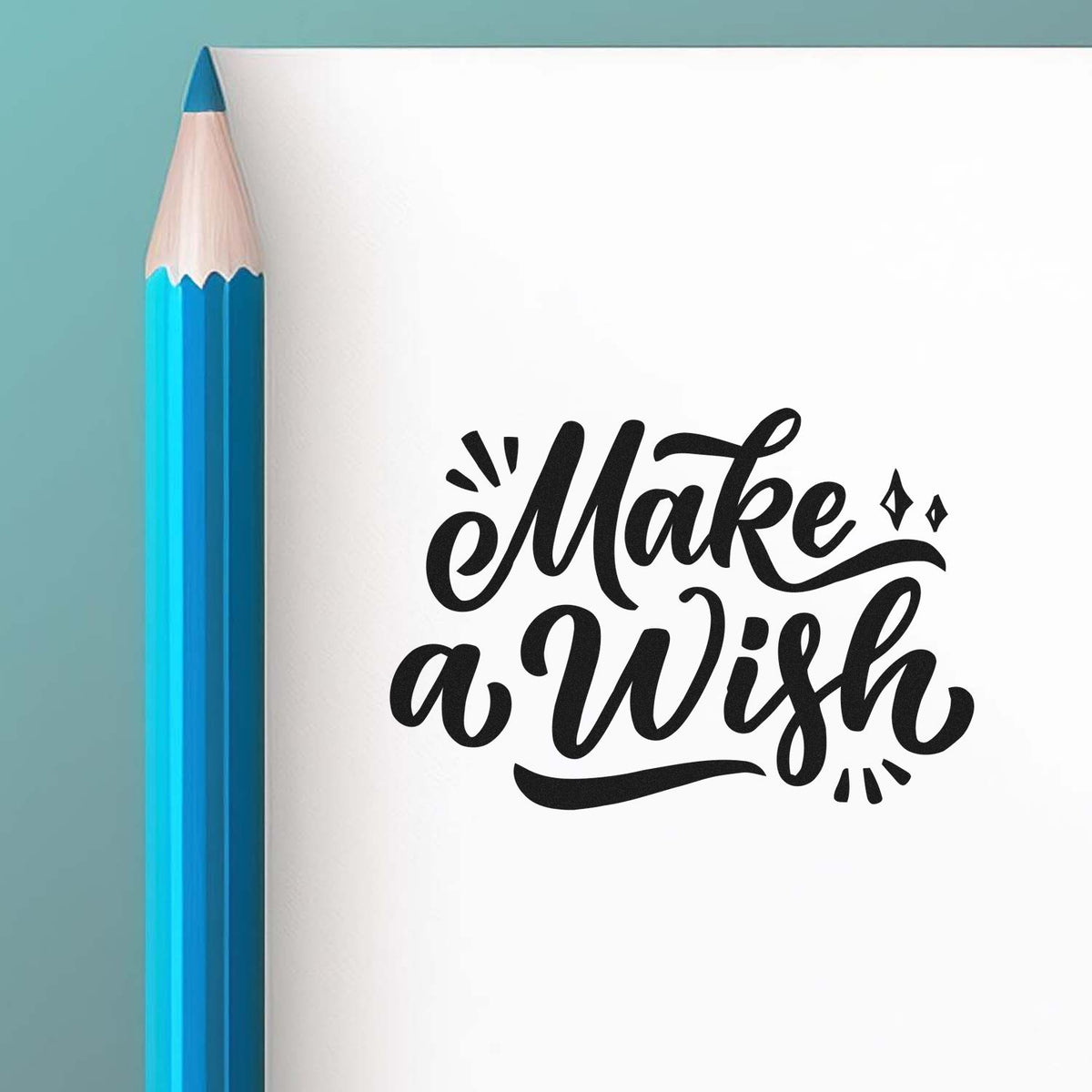 Black decorative Make a Wish stamp/seal on white paper beside a blue pencil, against a teal background.