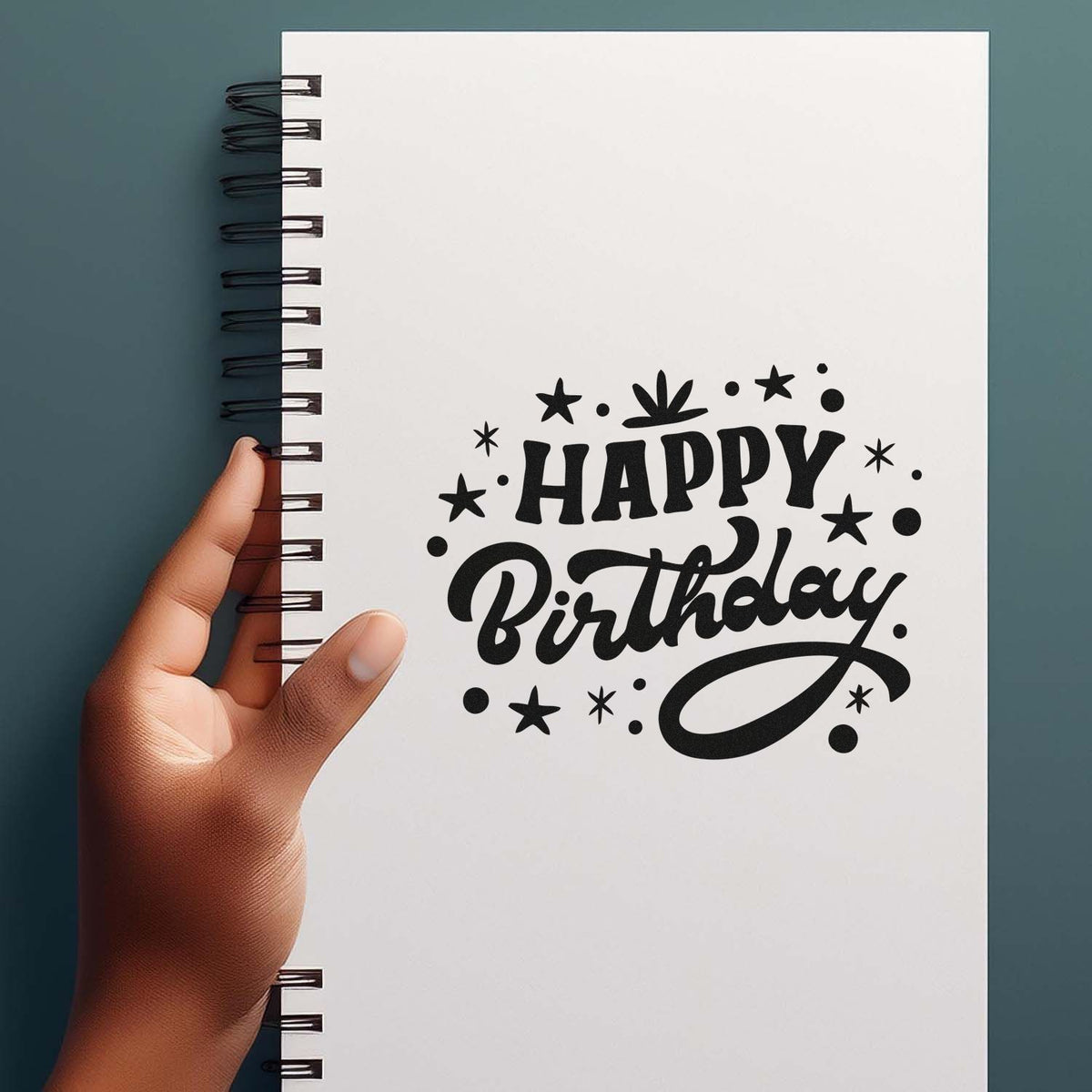 Black Happy Birthday stamp and seal design on white spiral notebook, with stars, dots, and a hand.