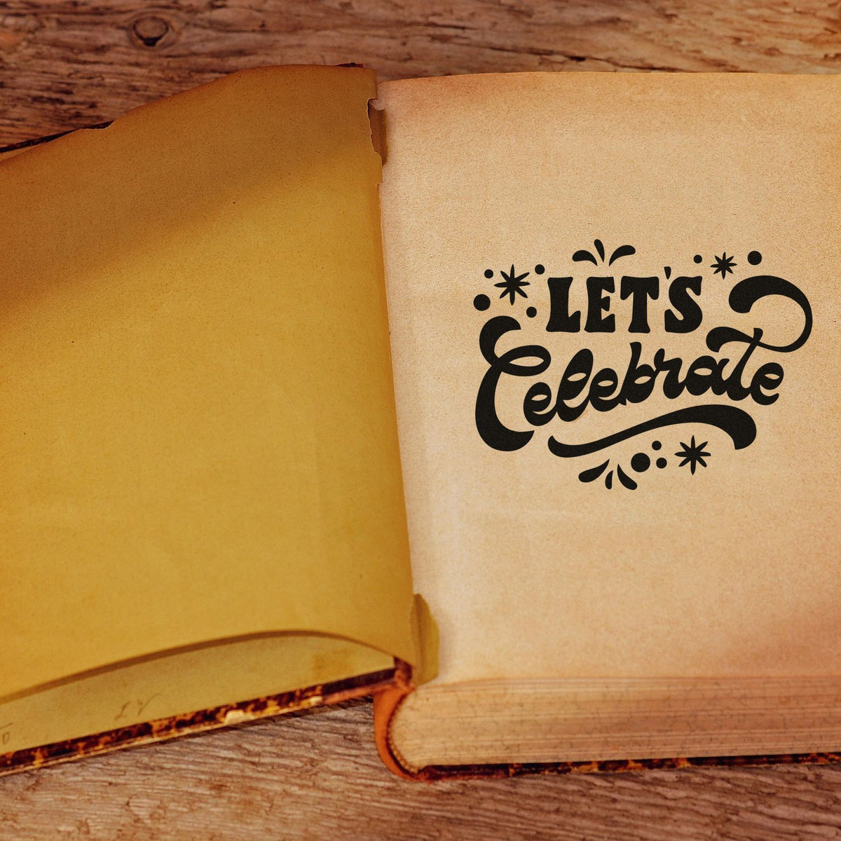 Custom stamp and seal design with black Lets Celebrate lettering on beige paper beside a warm yellow page on rustic wood.