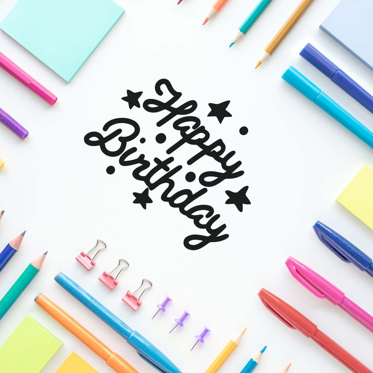 Black Happy Birthday stamp and seal with stars, surrounded by colorful pens, pencils, sticky notes, and binder clips.