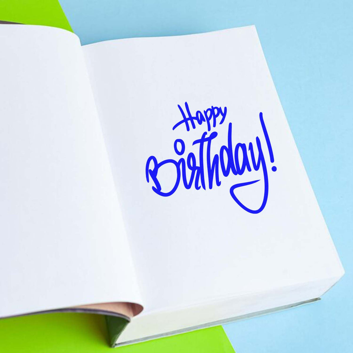 Blue Happy Birthday stamp seal on white paper, set against a light blue background with green accents.