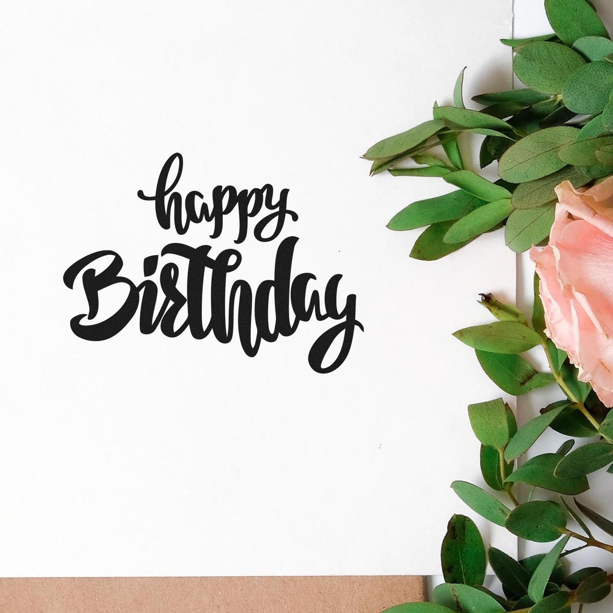 Black happy Birthday stamp/seal in bold script on white, framed by green leaves and pink flowers.