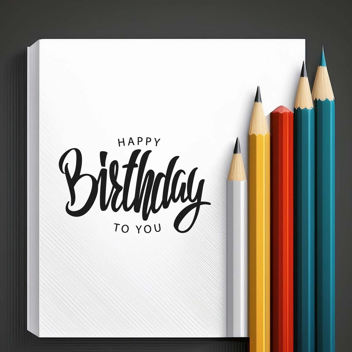 Happy Birthday stamp and seal on white card with black script, beside yellow, red, teal, and blue pencils.
