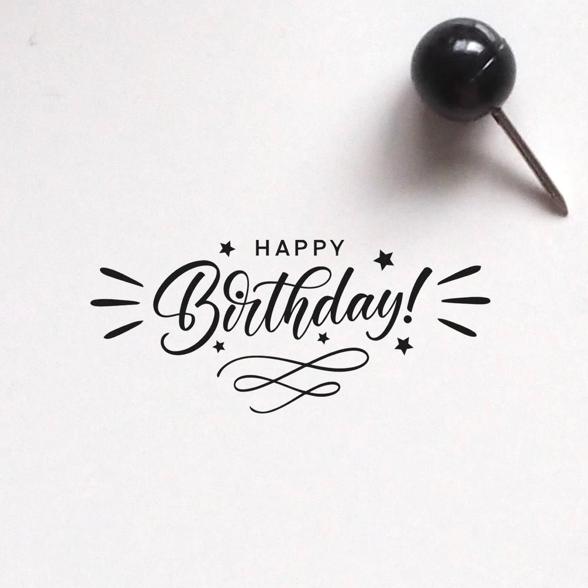 Black Happy Birthday stamp seal with stars and swirls, plus a black-handled pin, on a white background.