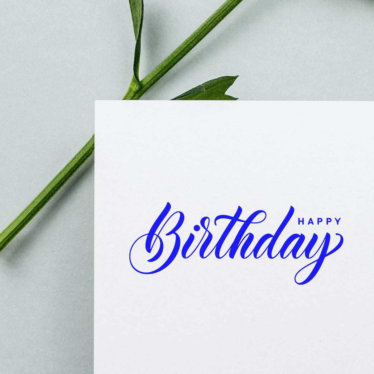 Blue Happy Birthday stamp on white card, with green stem and leaf, showcasing stamp and seal design.