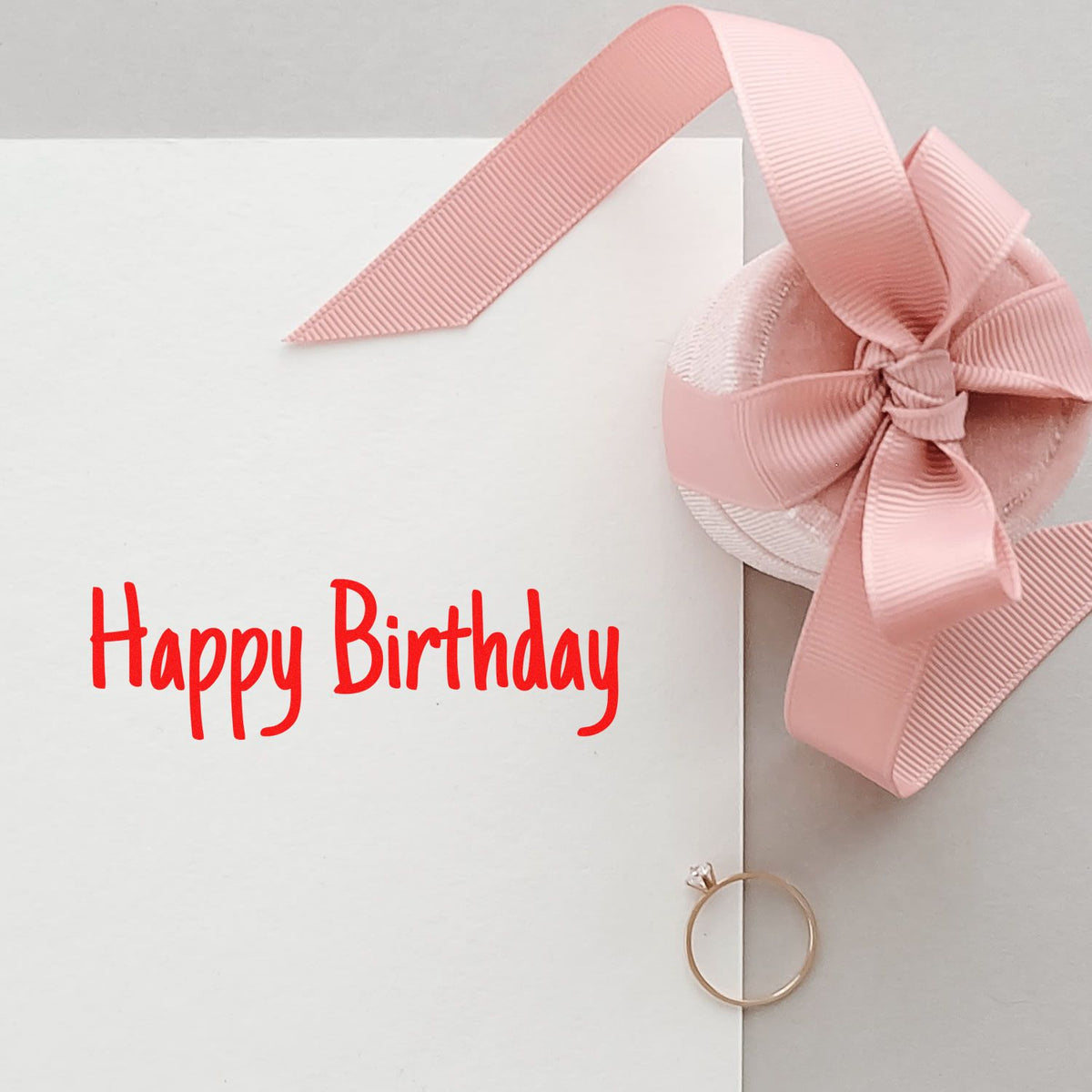 White birthday card with red Happy Birthday stamp and pink ribbon seal bow, plus gold ring accent.
