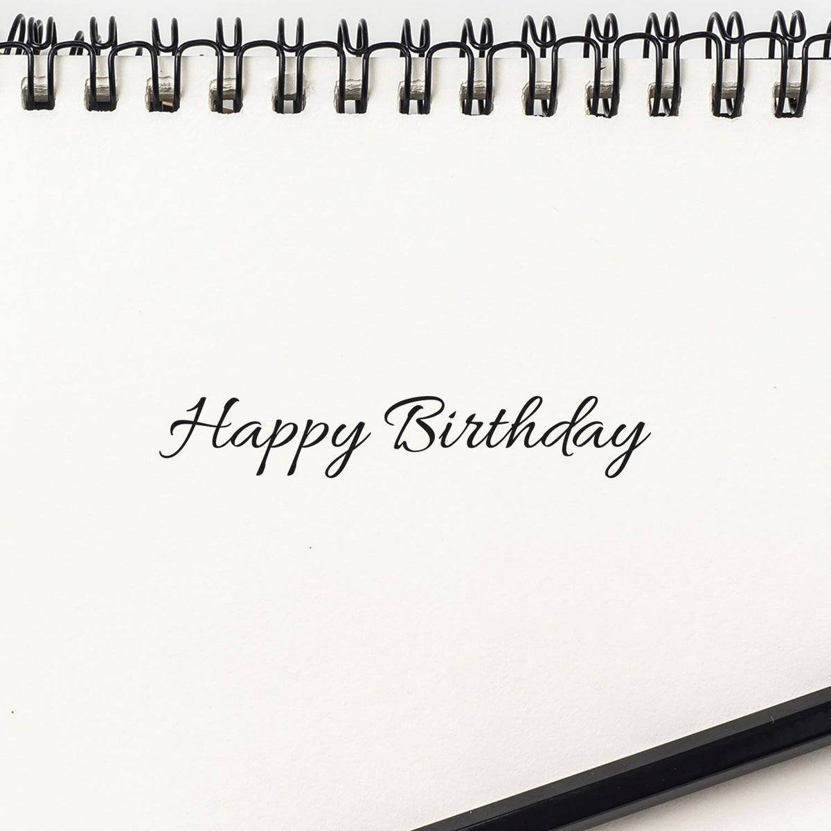 White spiral notebook page with black Happy Birthday cursive stamp, showcasing stamp and seal product design.