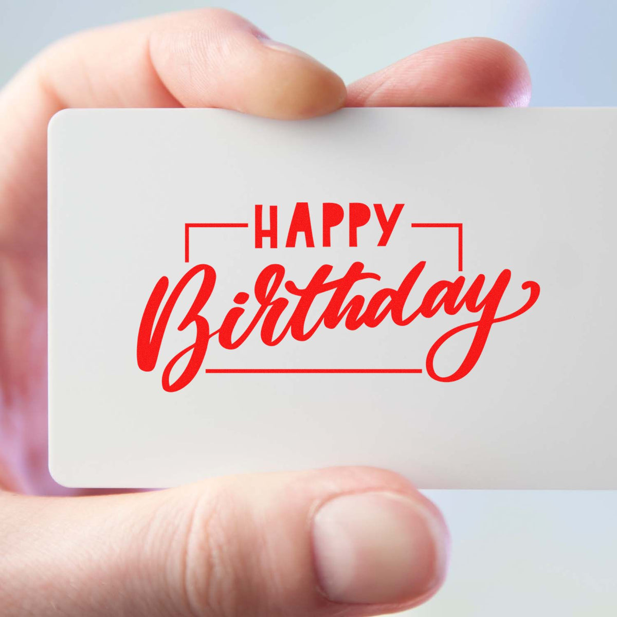 Hand holding white stamp card with red Happy Birthday seal in bold script and frame