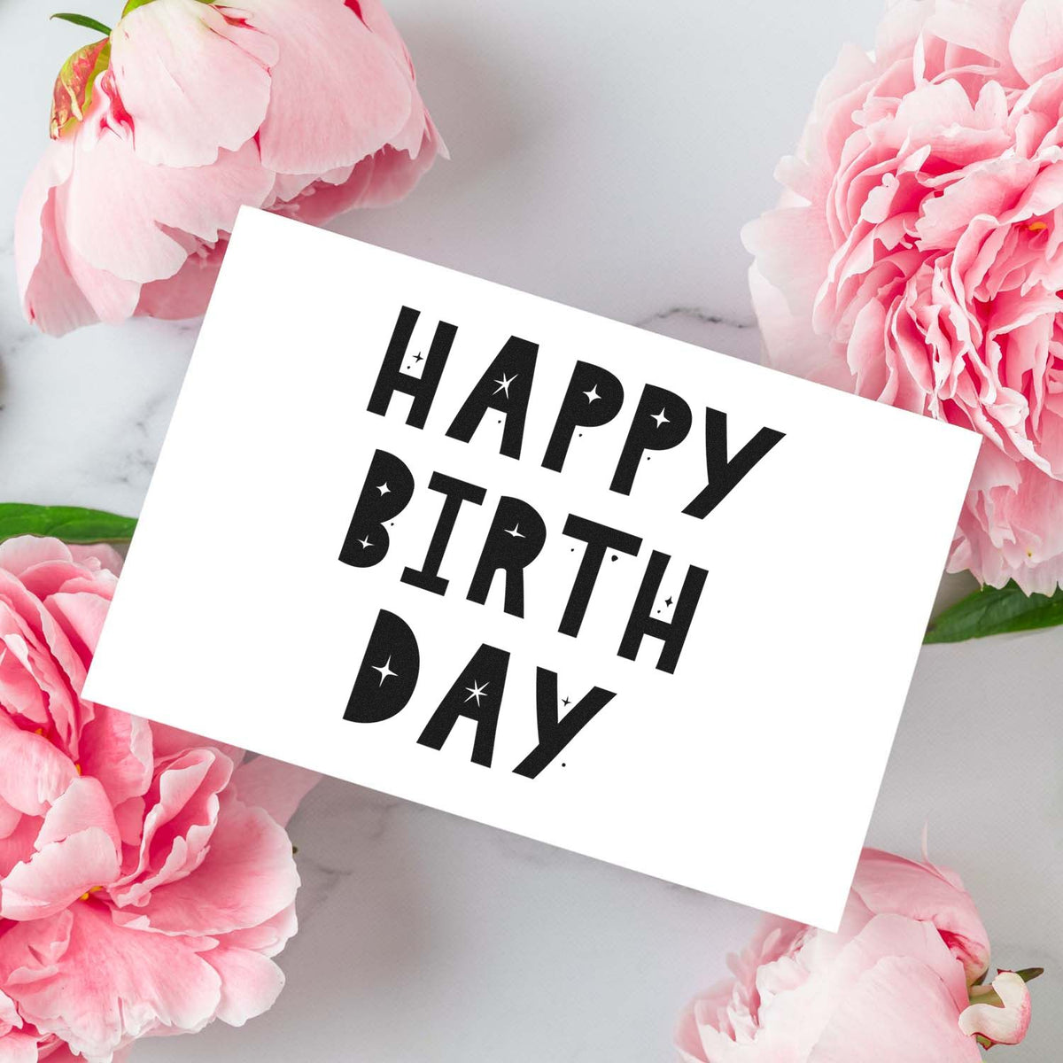 Happy Birthday stamp and seal design in bold black on white card, surrounded by pink peonies on a white marble background.