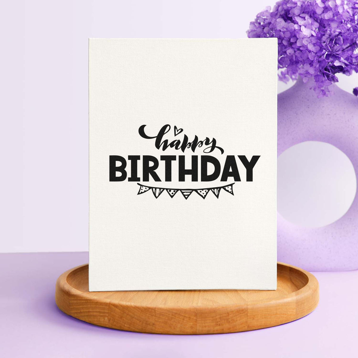 Black Happy Birthday stamp and seal on white canvas, with purple floral accent and wooden base.