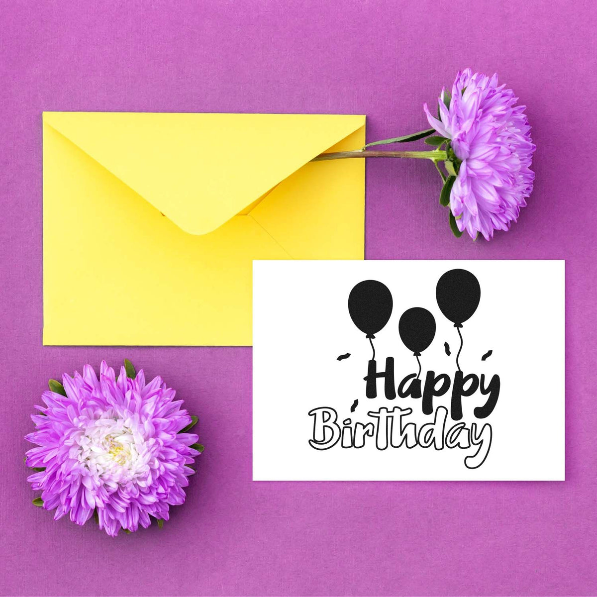 Black Happy Birthday balloon stamp and seal on white card, with yellow envelope and purple flowers on pink background.