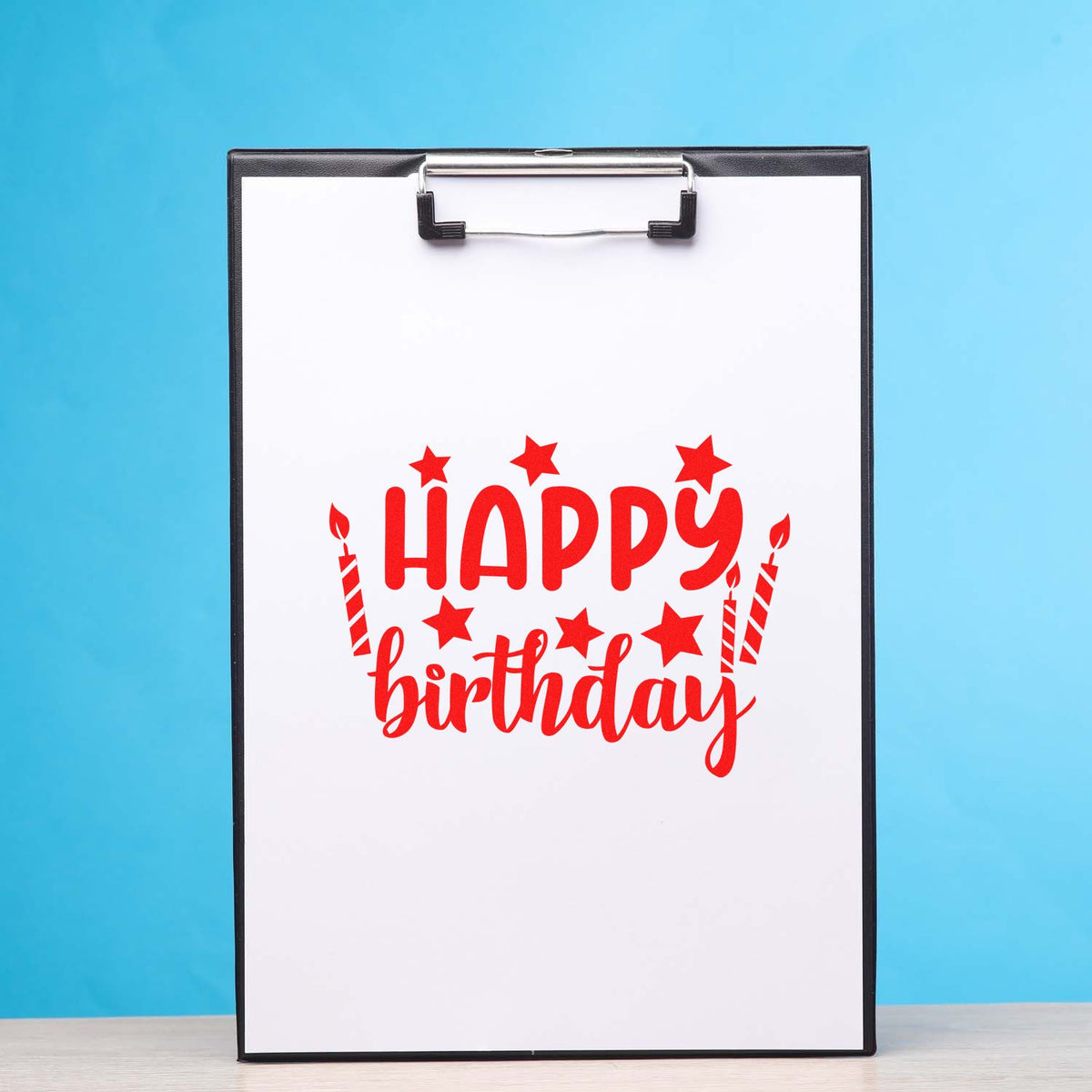 Red happy birthday stamp and seal design on a clipboard, with stars, candles, and a blue background.