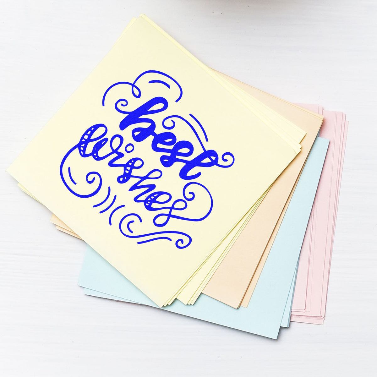 Stack of pastel paper sheets with a blue decorative stamp-and-seal design, featuring swirling script and flourishes.