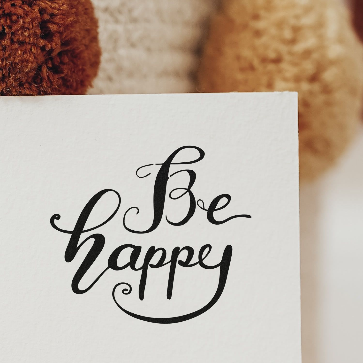 Black Be happy calligraphy stamp and seal on white paper, with a warm brown blurred background.