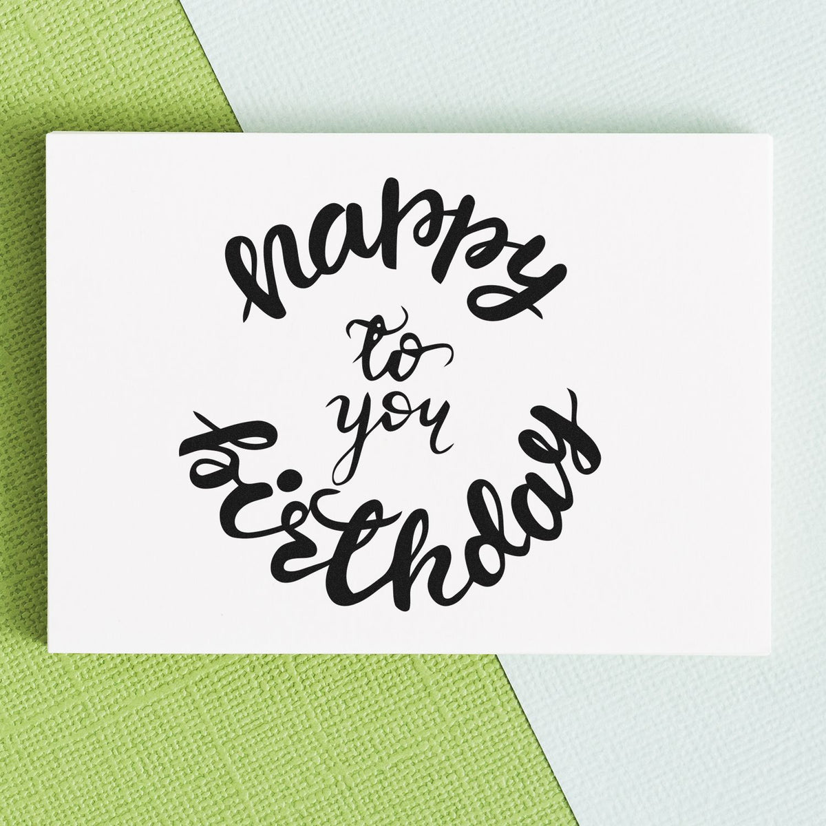 Black script happy to you stamp seal on a white square card, over a green and pale mint textured background.