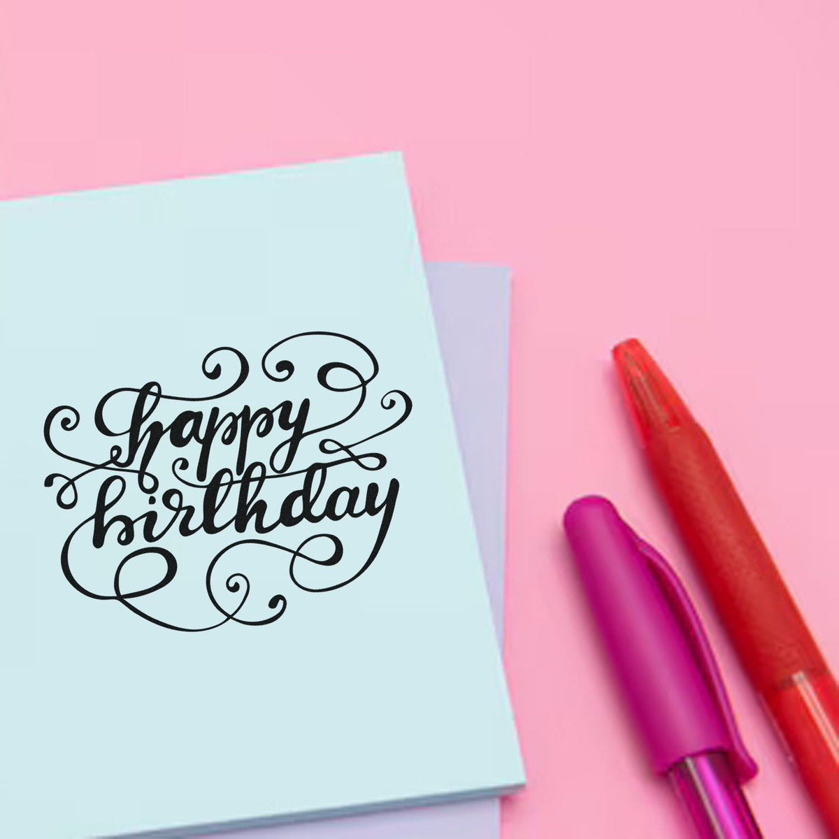 Happy birthday stamp and seal products on a light blue card, with black script and red and purple pens on a pink background.