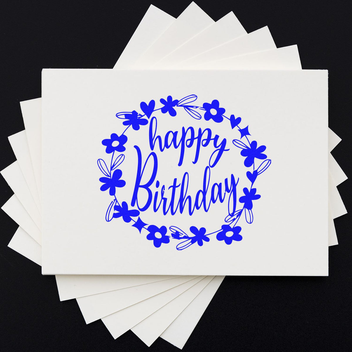 Blue happy birthday stamp and seal design with floral wreath on stacked white cards, set against a black background.