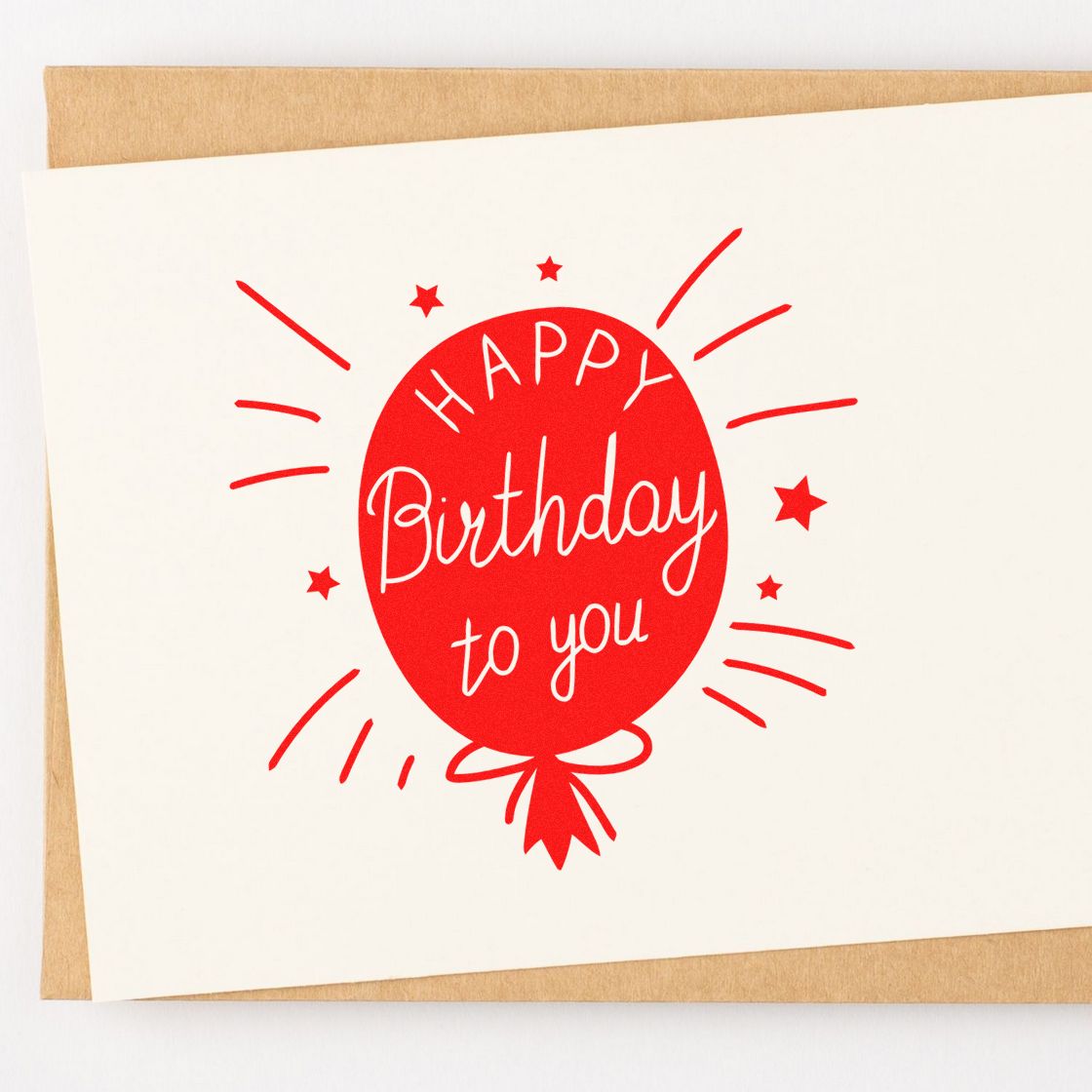 Red birthday balloon stamp-seal reading Happy Birthday to you on white card with kraft envelope background.
