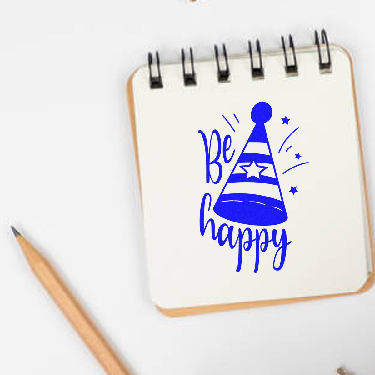 Blue Be happy party hat stamp design on a white spiral notebook, with stars and a pencil.